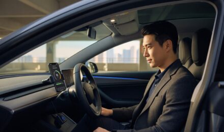 Smartphone displaying telematics driving score app next to a car steering wheel for usage based auto insurance