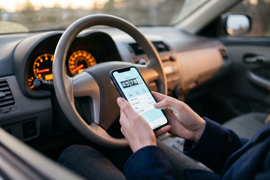 Person plugging OBD-II telematics device into car dashboard port for pay-per-mile insurance enrollment