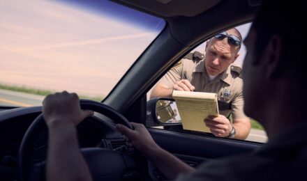 Driver holding expired insurance card at red light, illustrating risks of uninsured driving