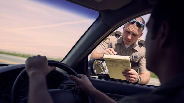 Driver holding expired insurance card at red light, illustrating risks of uninsured driving