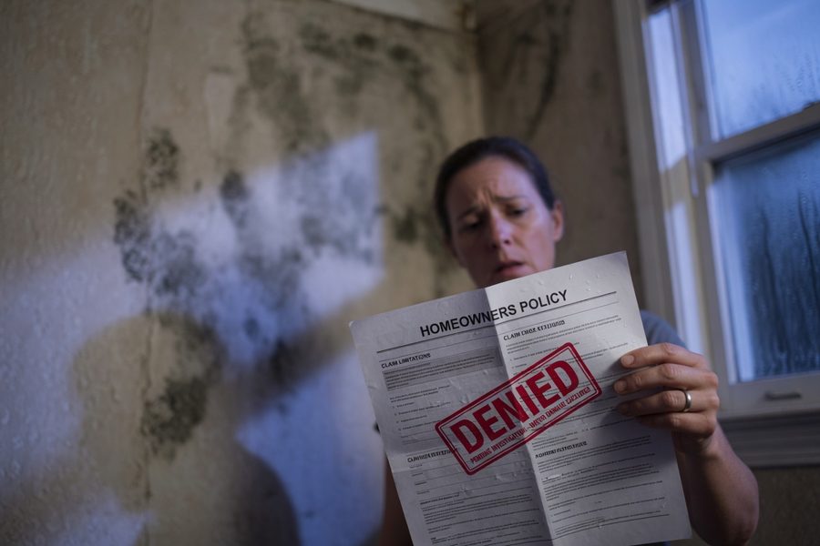 Homeowner reviewing a denied insurance claim letter at kitchen table after storm damage